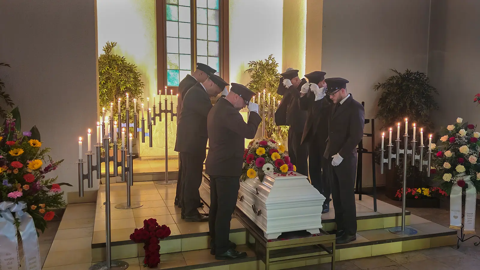 Erdbestattung in Berlin mit weißem Sarg, Blumenschmuck und professionellen Sargträgern in einer Trauerhalle