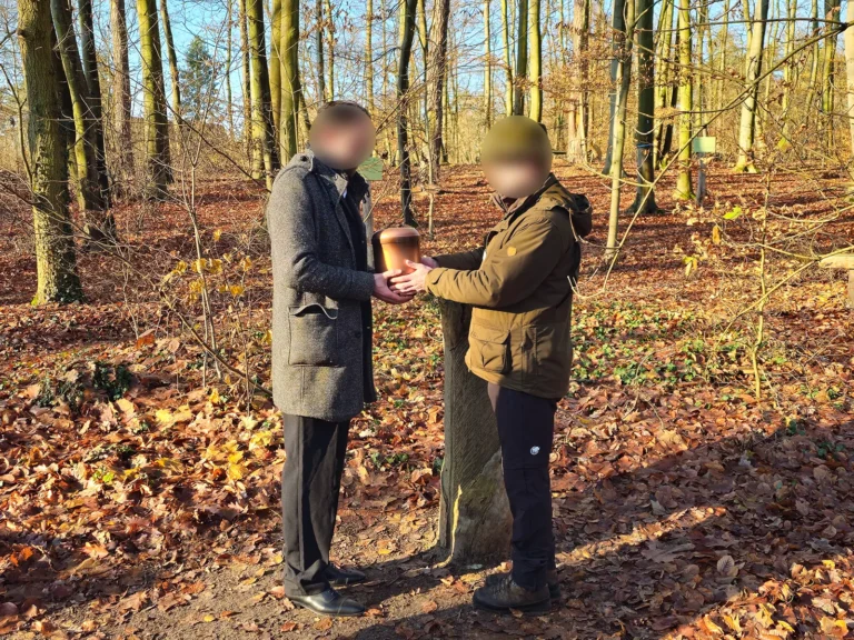 Angehöriger übernimmt eine Urne bei einer Waldbestattung in einem Bestattungswald